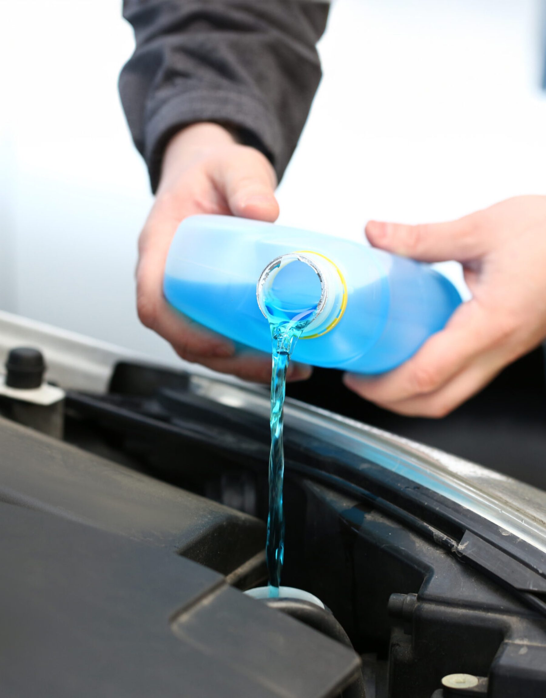 Male serviceman hands pouring blue washer fluid from a bottle into car concept